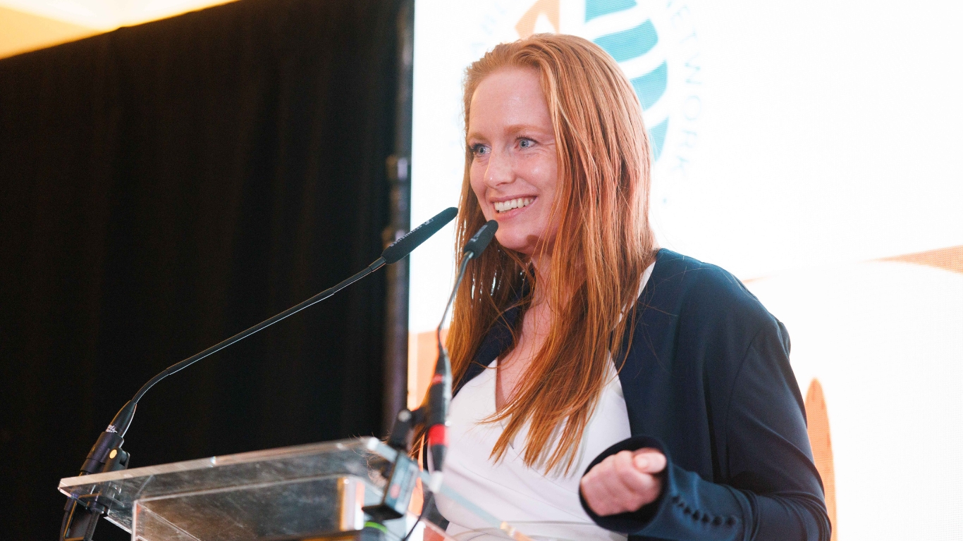 Red haired woman talking into a microphone while presenting and smiling