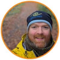 Darren Rice Geopark Manager. Smiling, red hair bearded man outside in nature wearing a blue Leave No Trace beanie hat, a yellow jacket and green scarf.