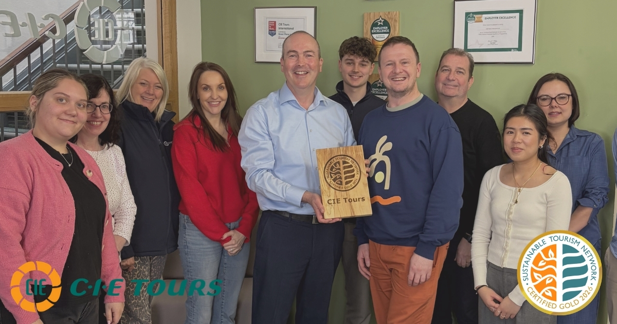 Group of people posing for a photo and smiling with a sustainable tourism certification wooden plaque. Sustainable Tourism Network Gold Certification logo. CIE Tours logo.